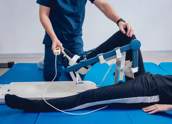 Fisioterapeuta asistiendo a paciente en equipo movilizador pasivo de rodilla para rehabilitación y movilidad articular — Equipos de rehabilitación